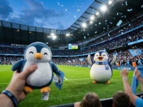 A fan holds a penguin plush toy at Etihad Stadium with a penguin mascot on the pitch and blue confetti falling