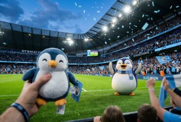 A fan holds a penguin plush toy at Etihad Stadium with a penguin mascot on the pitch and blue confetti falling