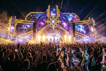 Large crowd at Celestial Sounds music festival facing a space-themed stage with lasers and pyrotechnics