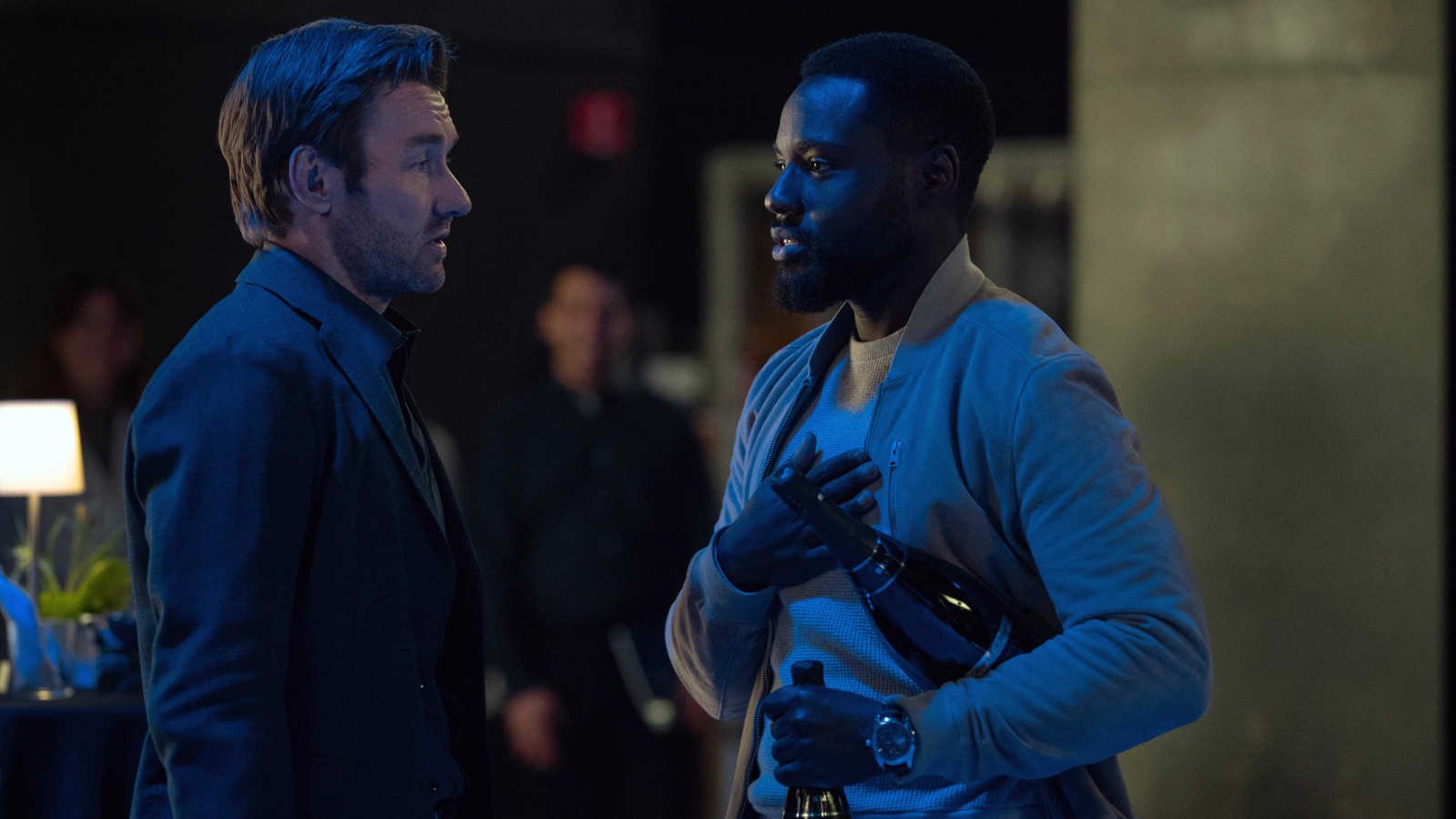 Jason Dessen (Joel Edgerton) talks to Leighton Vance (Dayo Okeniyi), who is carrying two bottles of champagne in Dark Matter season 2