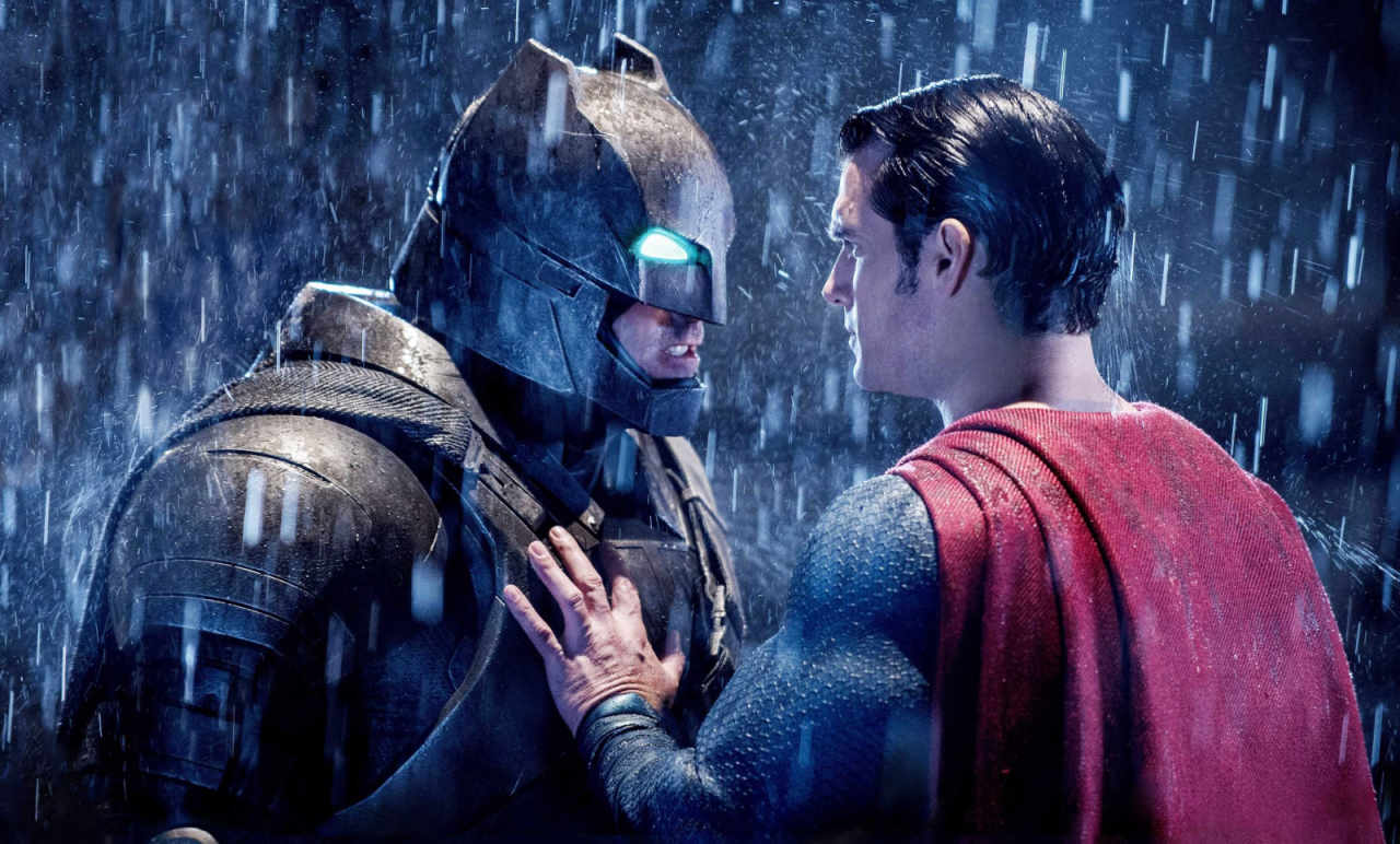 Batman, in a robotic Batsuit, stares down Superman with a glowing glare as rain falls around them in an image from Batman v Superman Dawn of Justice.